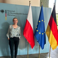 Emilie Funken in der deutschen Botschaft in Warschau neben drei Flaggen: von Polen, der Europöischen Union und Deutschland